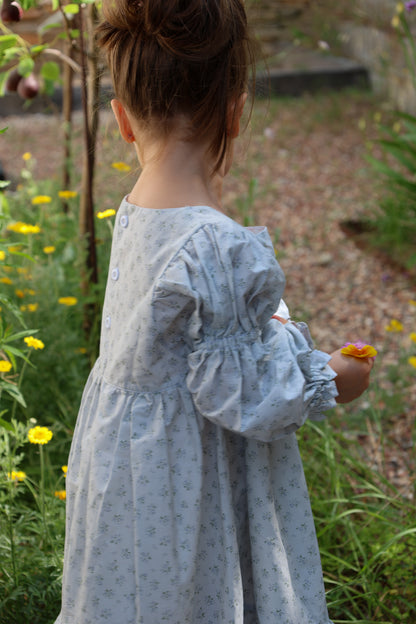 Child in a light blue dress standing in a garden with flowers.