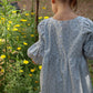 Child in a light blue dress standing in a garden with yellow flowers.