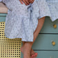 Person wearing a light blue floral dress sitting on a green dresser.