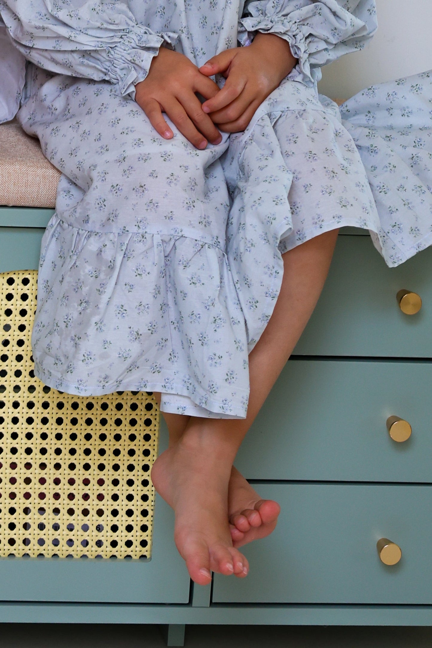 Person wearing a light blue floral dress sitting on a green dresser.