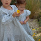 Two young girls in light blue dresses standing in a garden with flowers.