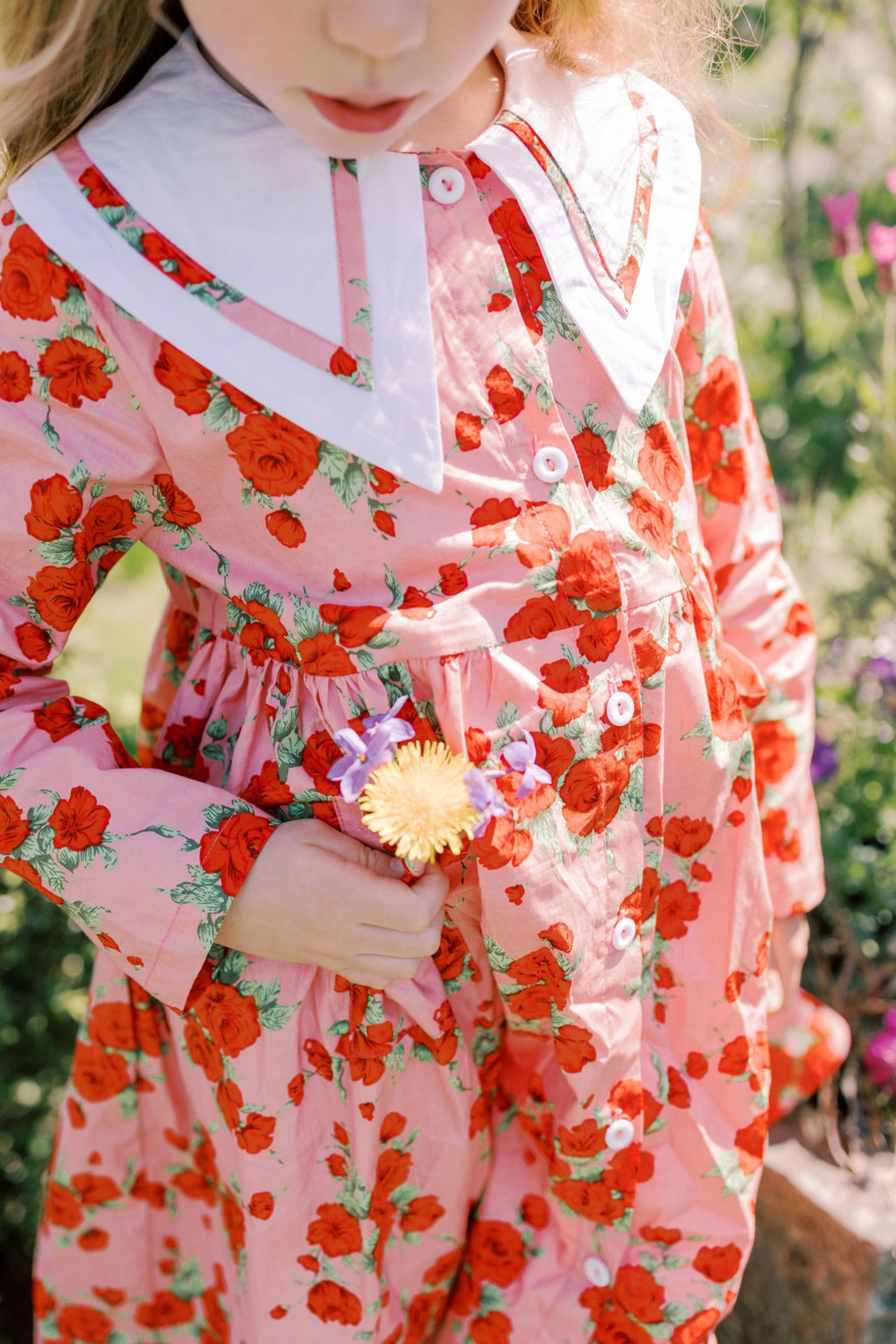 Child wearing a pink floral dress holding a colorful flower in a garden setting