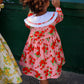 Child wearing a pink floral dress standing next to a green wall.