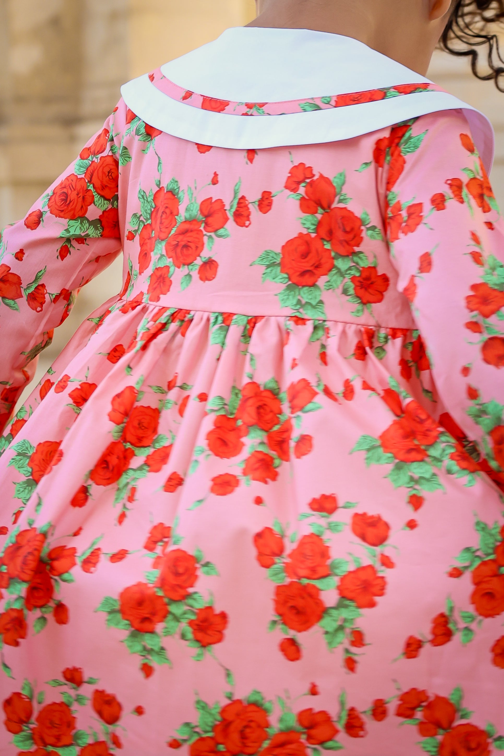 Pink dress with red floral pattern worn by a child