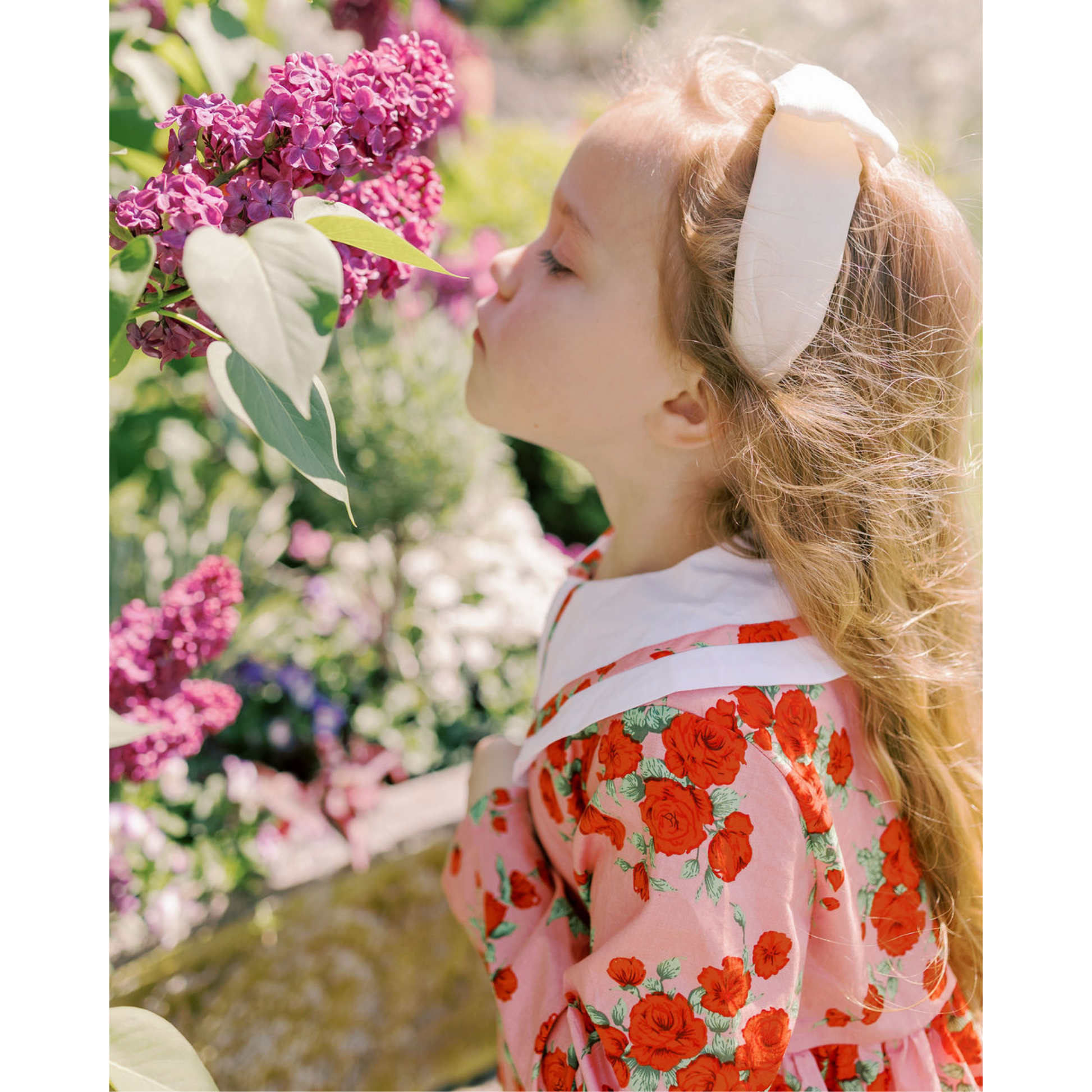 Young girl smelling a pink flower in a garden