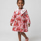 Child wearing a pink floral dress with a white collar on a white background