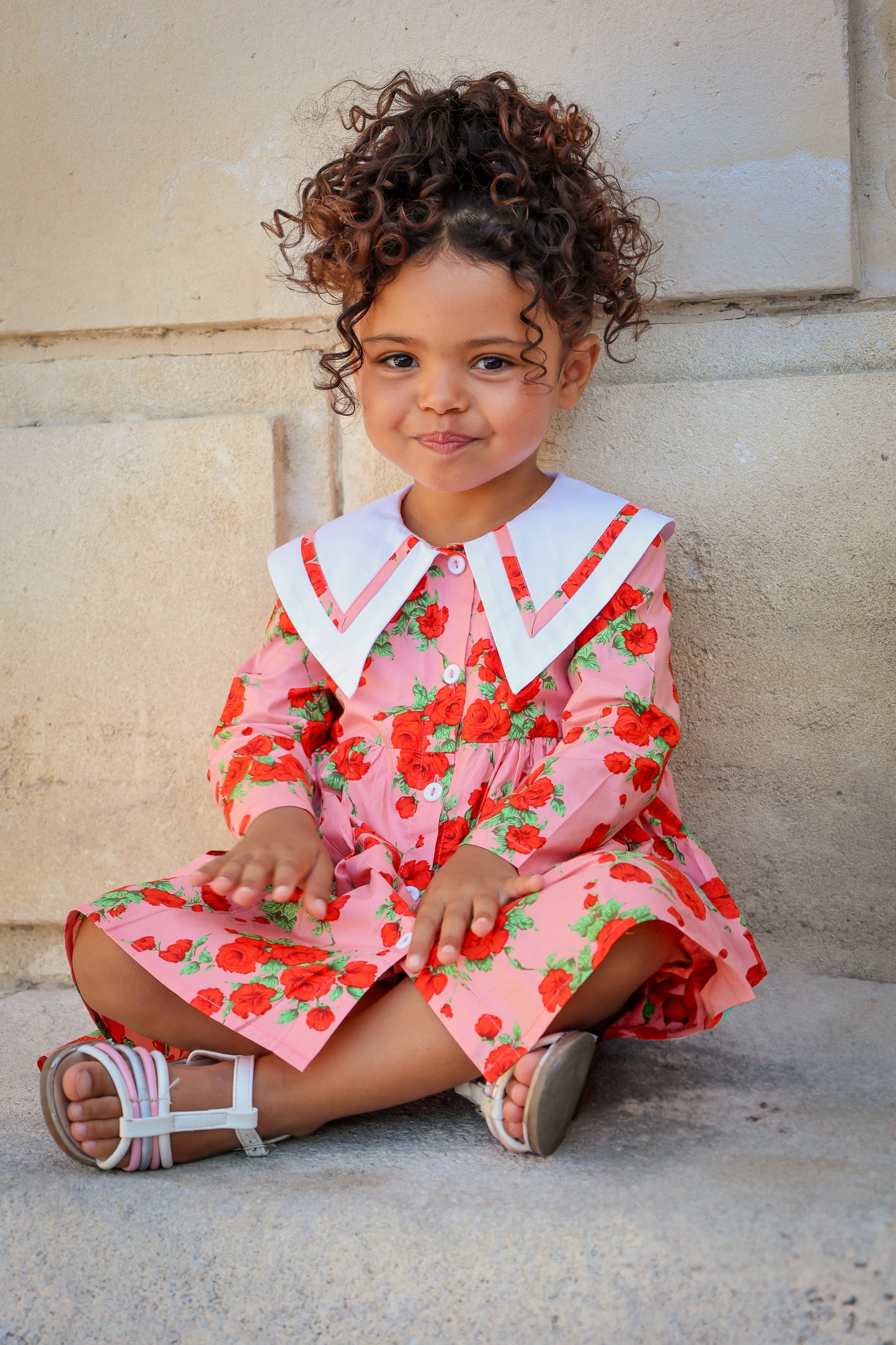 Young girl in a floral dress sitting on steps.