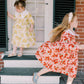 Two young girls in floral dresses standing on a set of steps outside a house.