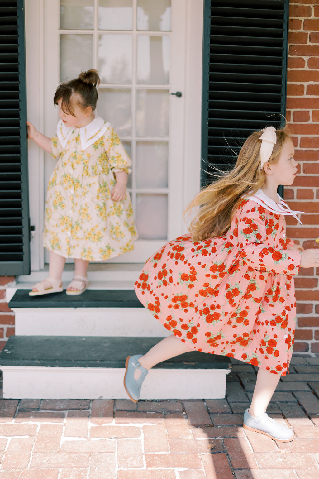 Two young girls in floral dresses standing on a set of steps outside a house.