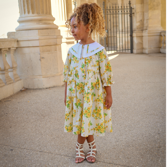 Young girl in a floral dress standing on a stone path with classical architecture in the background