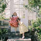 Two children in colorful dresses standing on stone steps in a greenhouse.