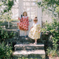 Two children in dresses standing on stone steps in a garden setting.