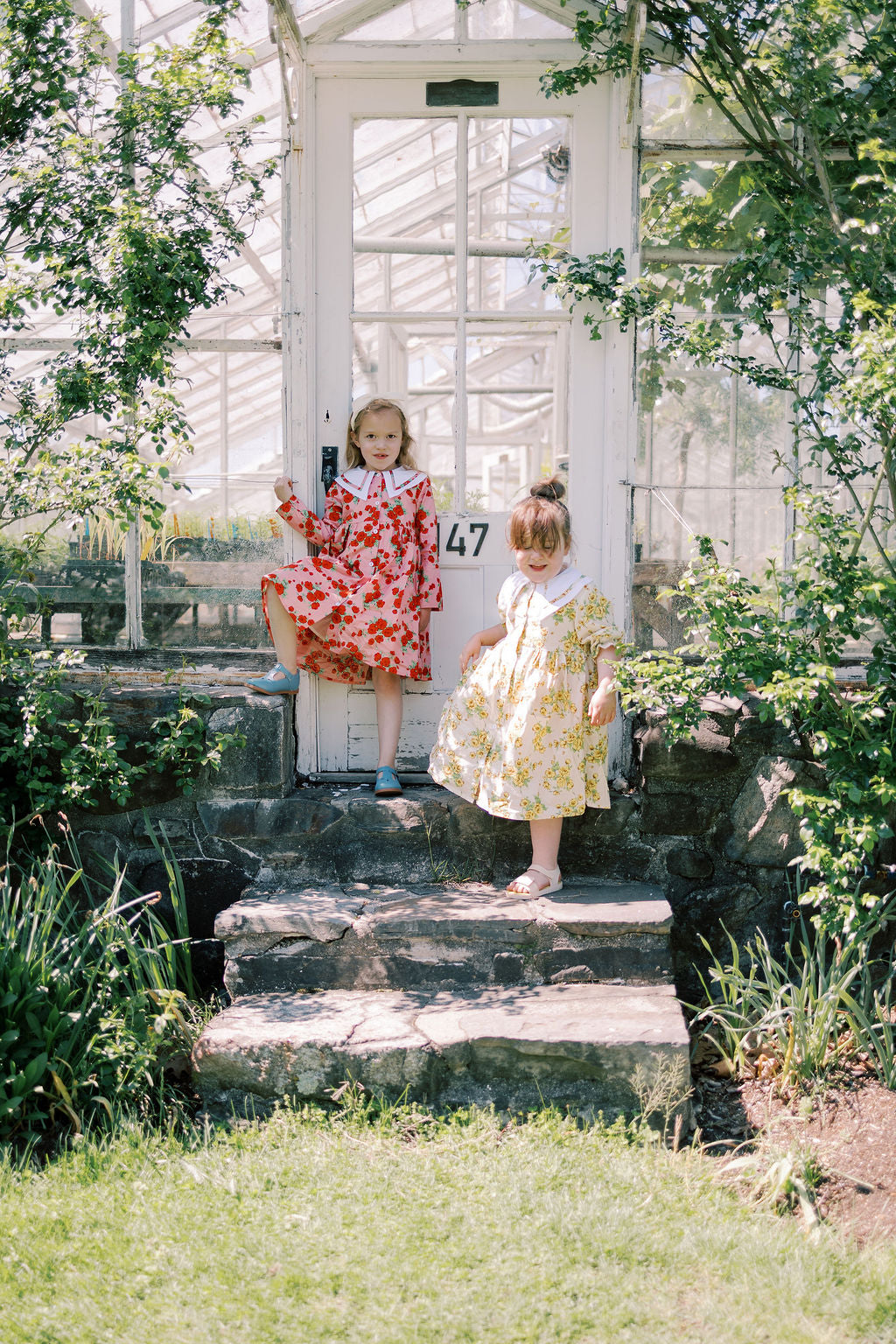 Two children in dresses standing on stone steps in a garden setting.
