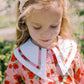 Young girl wearing a floral dress with a large bow in her hair, standing outdoors.