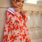 Child wearing a pink floral dress standing against a stone wall.