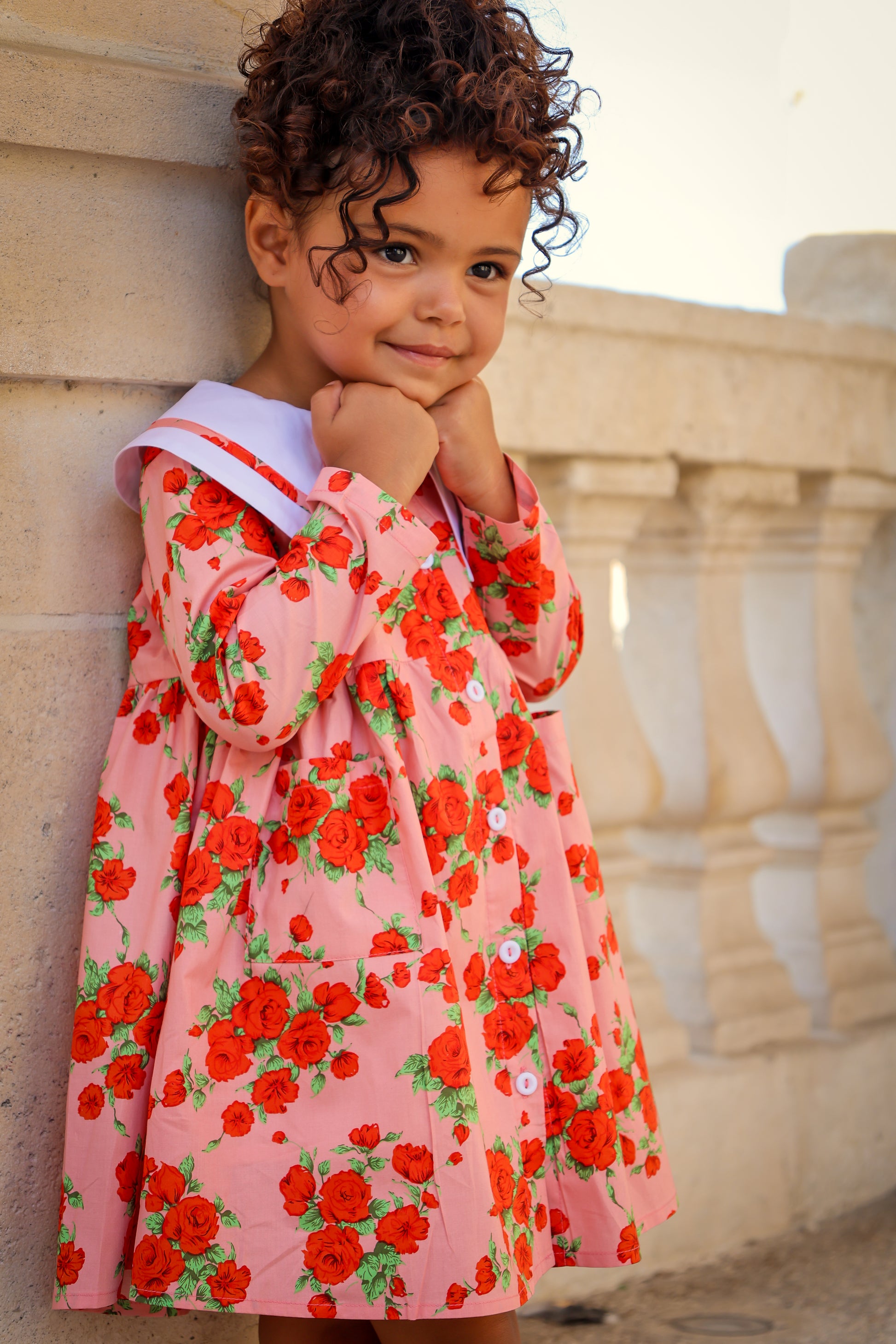 Child wearing a pink floral dress standing against a stone wall.