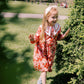 Young girl in a red floral dress standing on grass with trees in the background