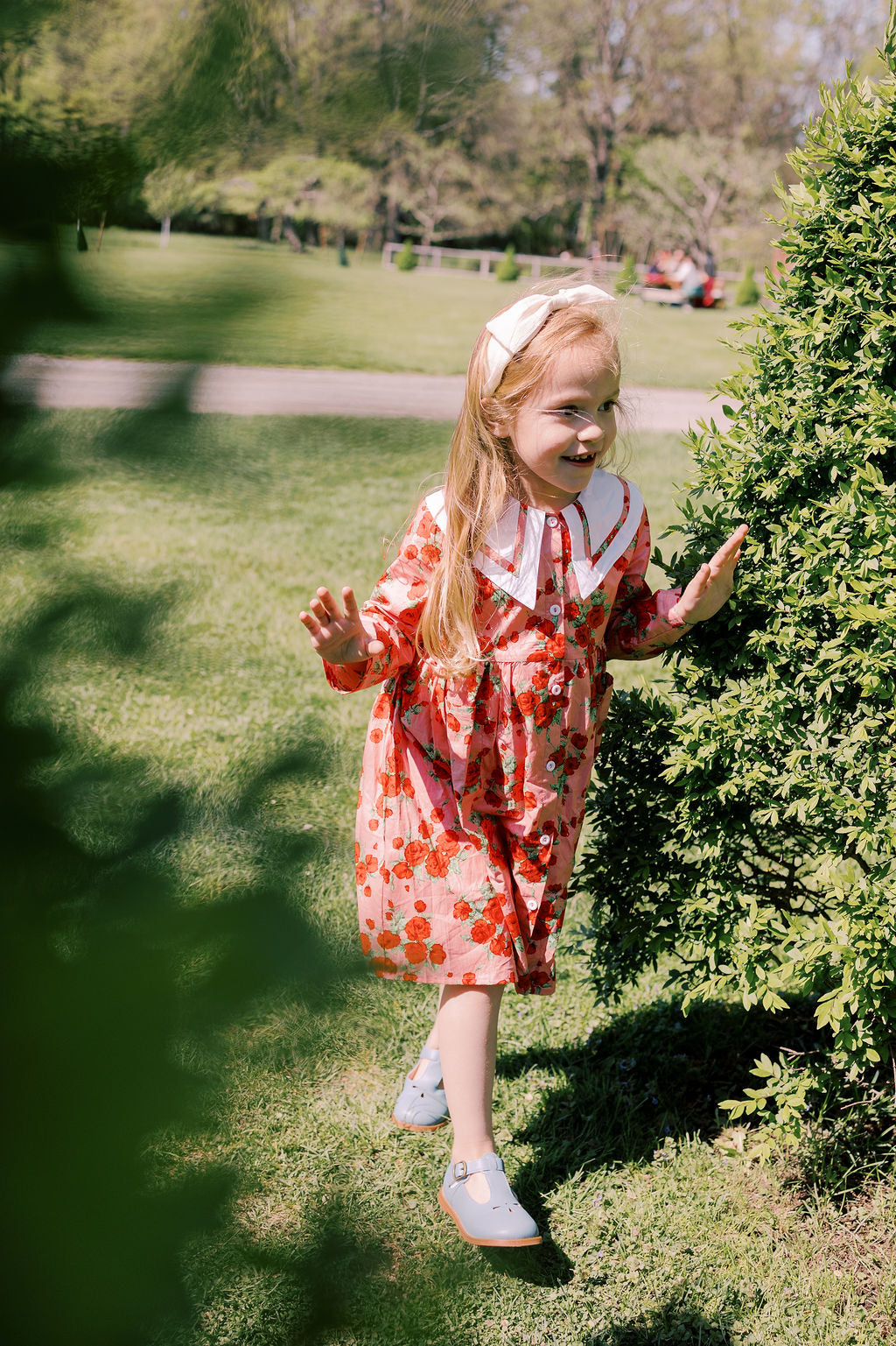 Young girl in a red floral dress standing on grass with trees in the background
