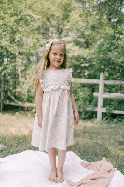 Young girl in a white dress standing outdoors with greenery in the background