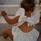 Baby in a floral outfit with a large bow sitting on stone steps.