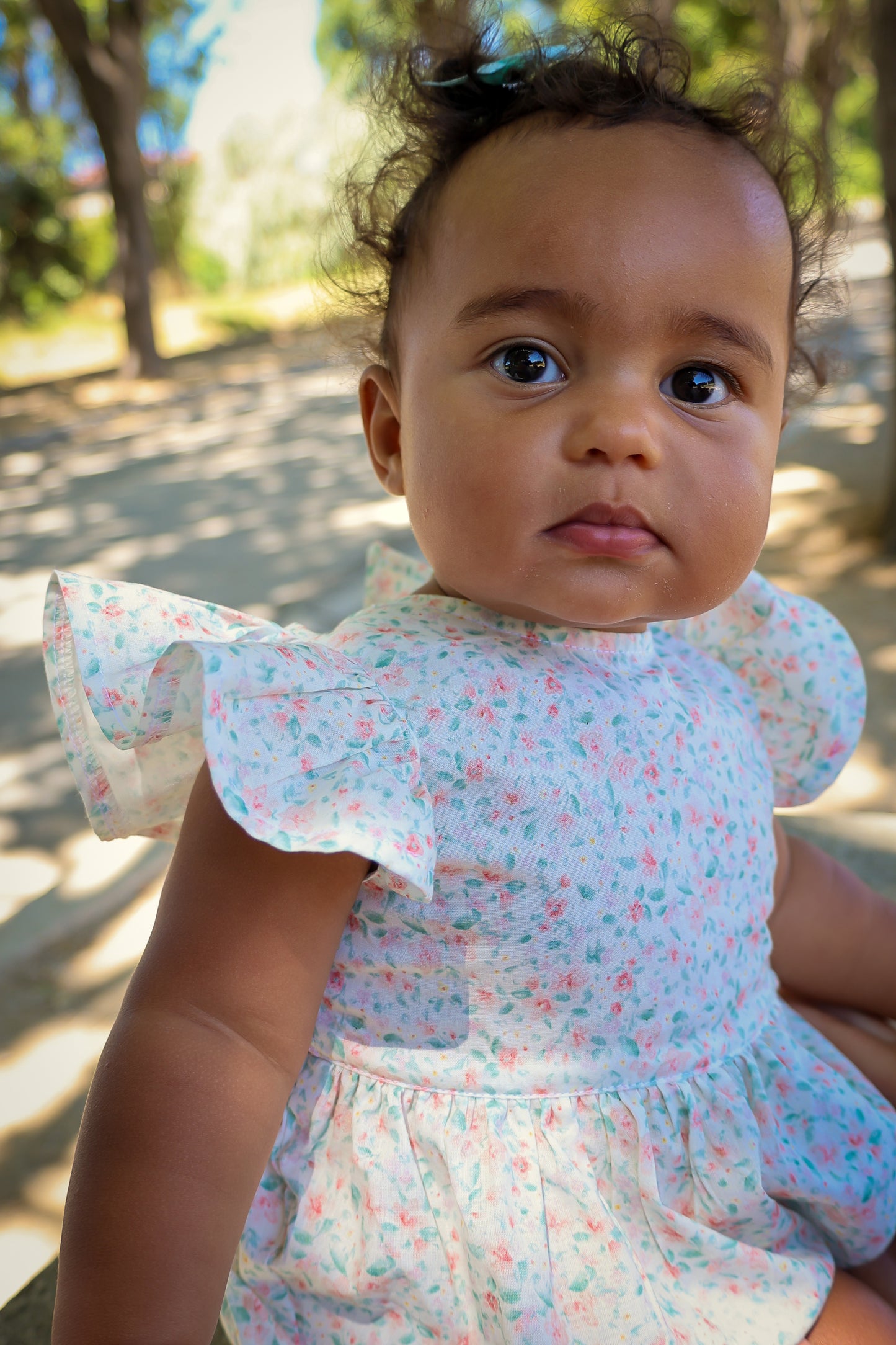 Baby wearing Confetti Print Josie Bubble sitting outdoors with trees in the background