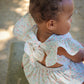 Baby in a Confetti print Josie Bubble sitting on a stone surface with a blurred natural background