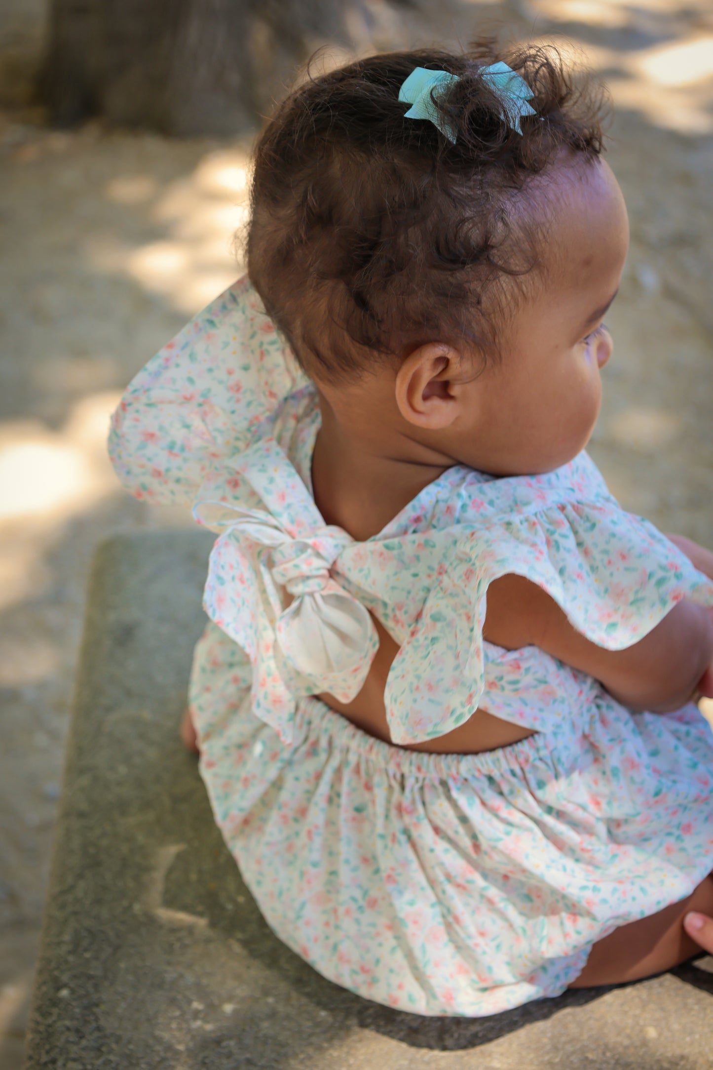Baby in a Confetti print Josie Bubble sitting on a stone surface with a blurred natural background