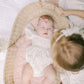 Baby in a crib with a pink bow, surrounded by a person in the Josie Confetti Print Bubble on a grassy background.
