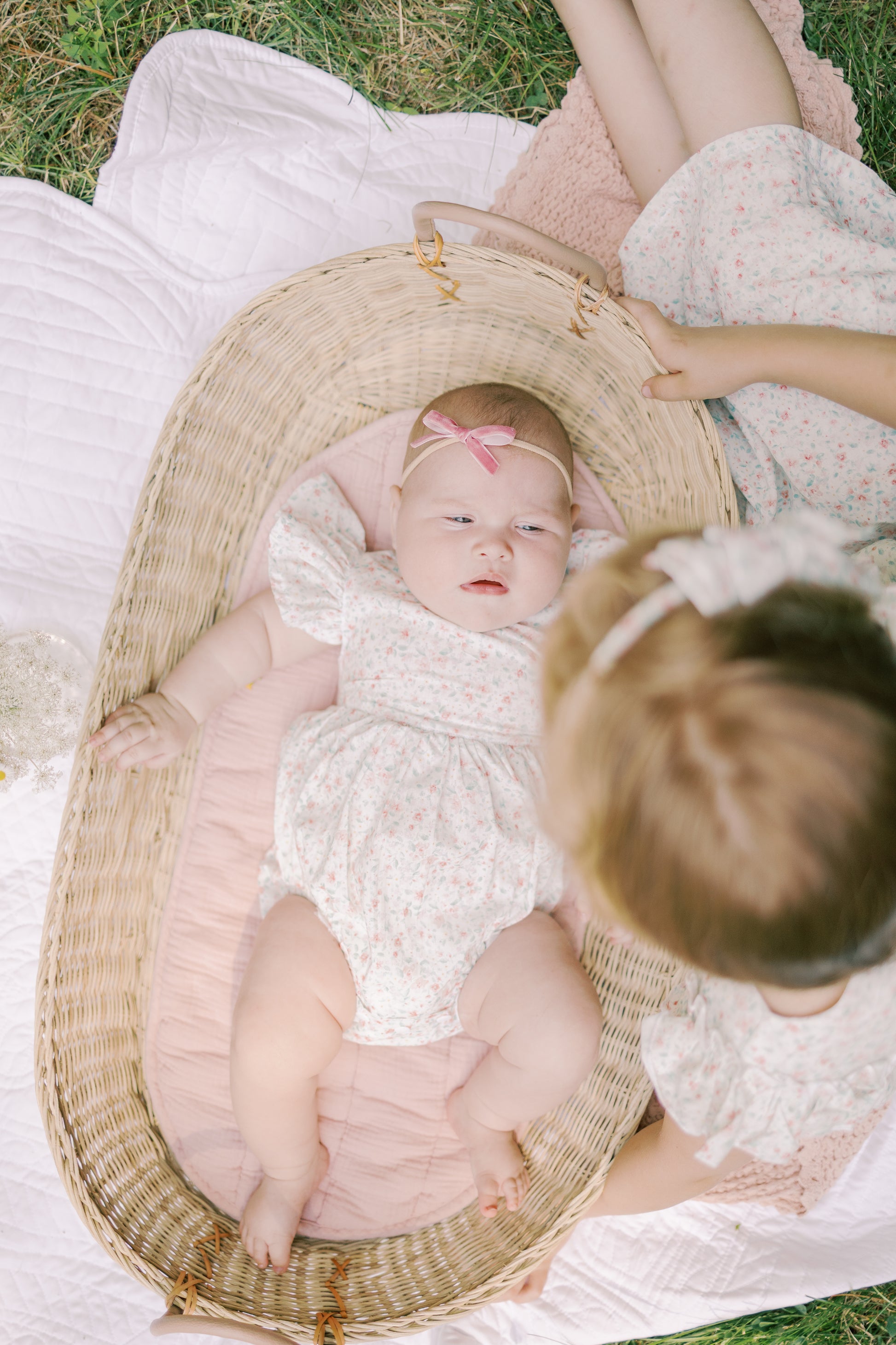 Baby in a crib with a pink bow, surrounded by a person in the Josie Confetti Print Bubble on a grassy background.