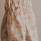 A young girl wearing a pink floral cotton dress with bell sleeves, holding a pink flower, with her hair styled in a bun.