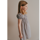 A young girl wearing a short sleeve muted purple dress with cap sleeves, standing against a neutral background.