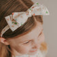 A child with a head circumference fitting for an adjustable headband with a multicolored heart pattern.