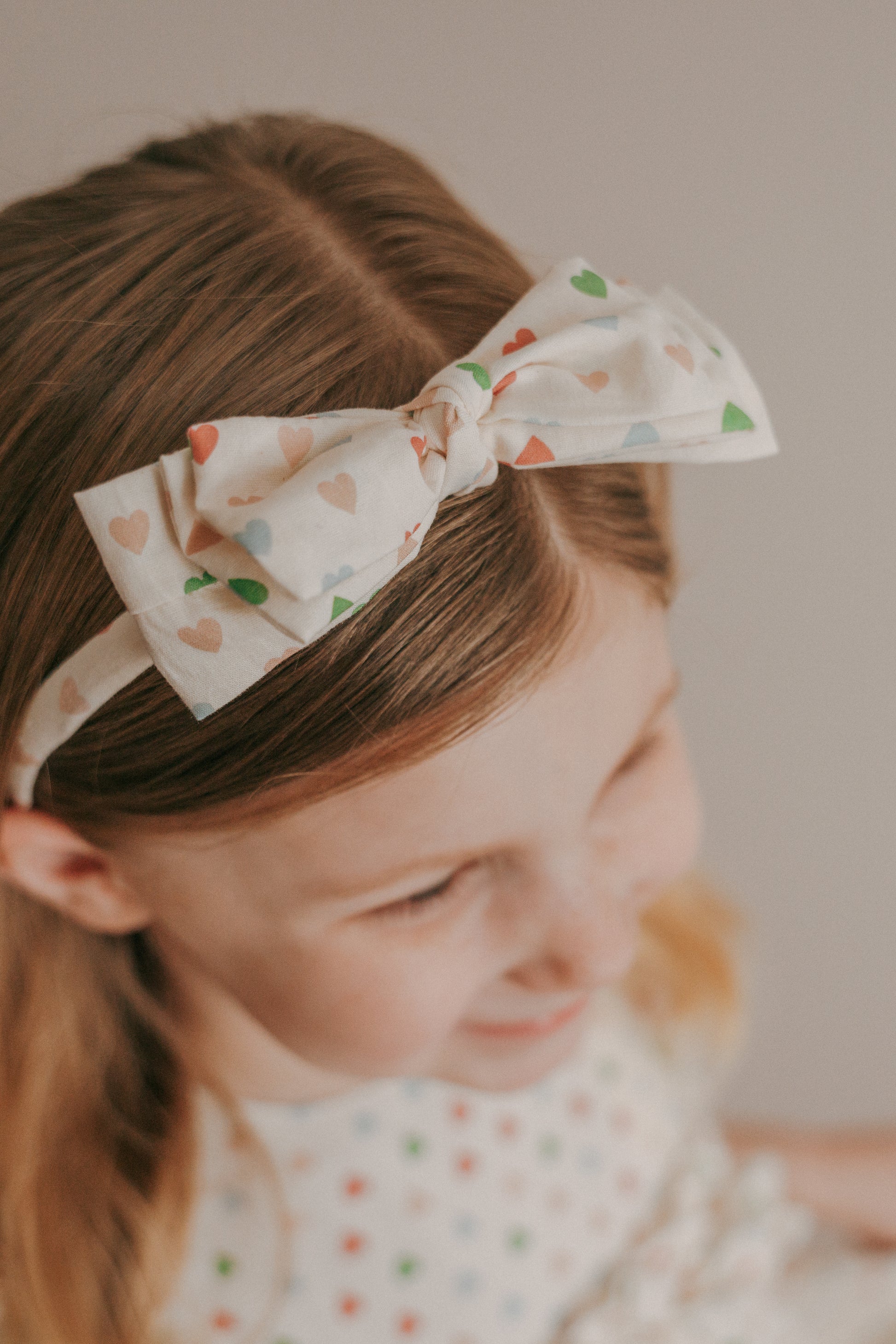 A child with a head circumference fitting for an adjustable headband with a multicolored heart pattern.