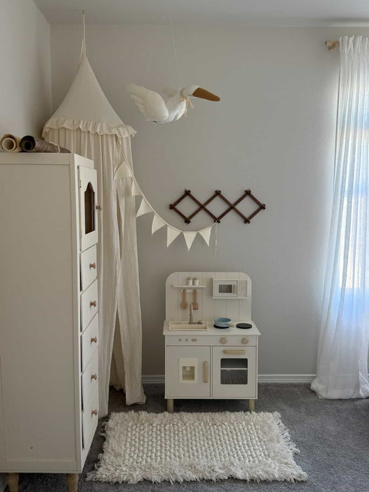 Children's playroom with a white toy kitchen, dresser, and decorative elements.