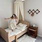 Child playing on a bed in a bedroom with a canopy and side table.