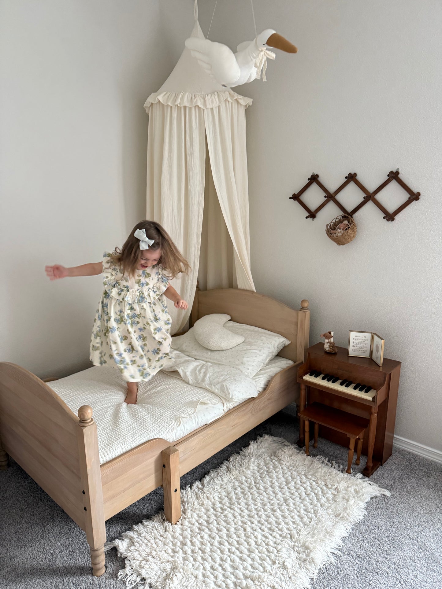 Child playing on a bed in a bedroom with a canopy and side table.