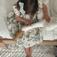 Child in a floral dress sitting on a bed with a wooden hanger.