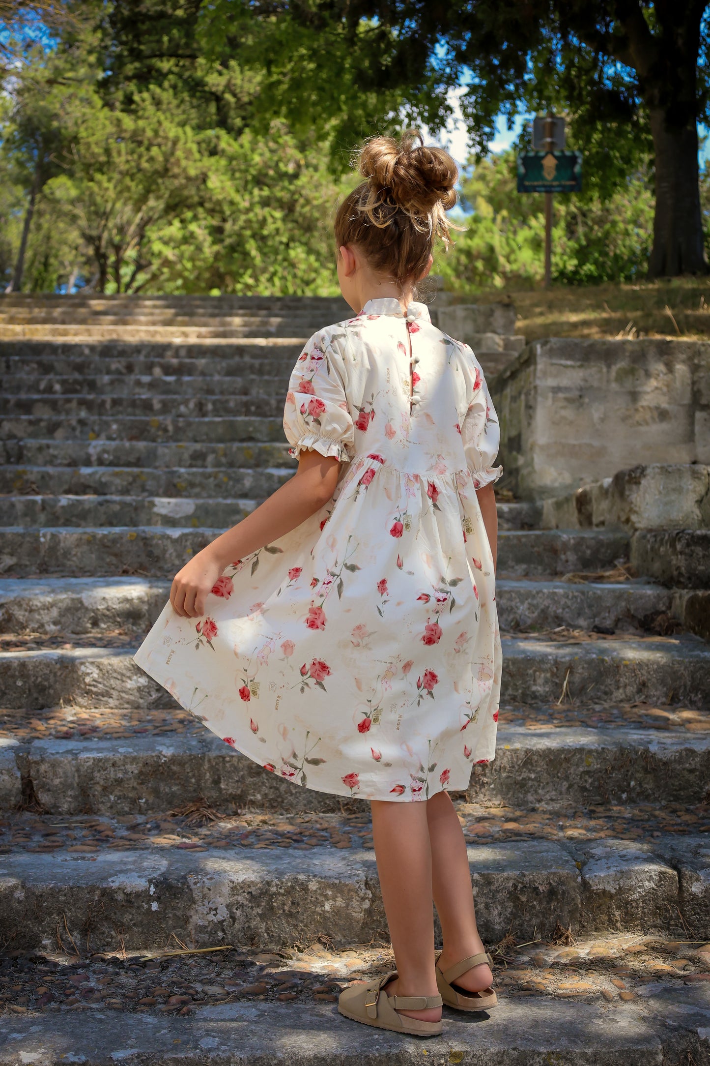 Young girl in a floral dress standing on stone steps outdoors