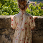 Woman in a floral dress standing against a stone wall with greenery in the background
