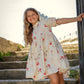 Young girl in a floral dress standing on stone steps outdoors