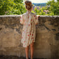 Woman in a floral dress standing against a stone wall with a scenic view in the background