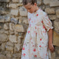 Young girl in a floral dress standing against a stone wall