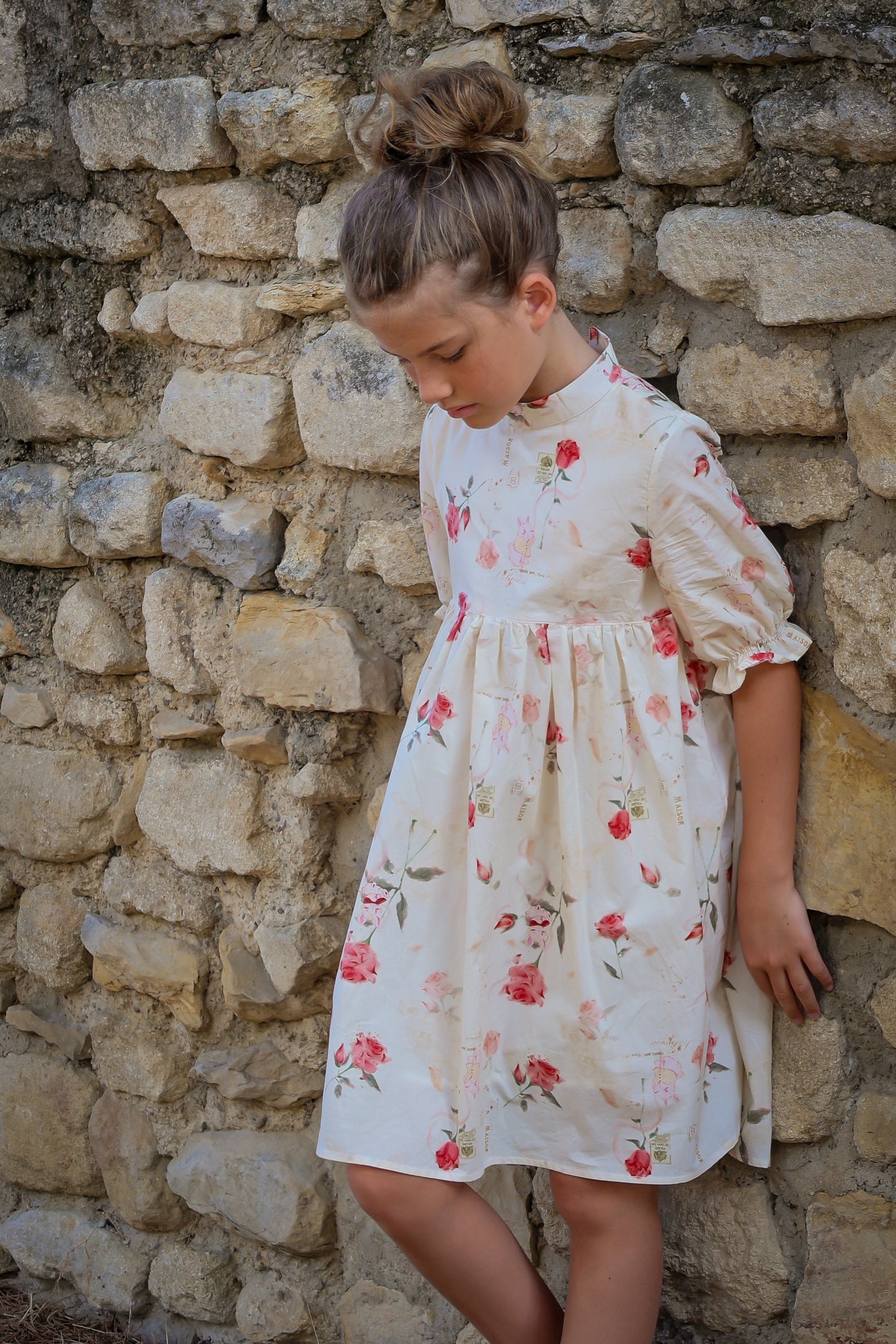 Young girl in a floral dress standing against a stone wall