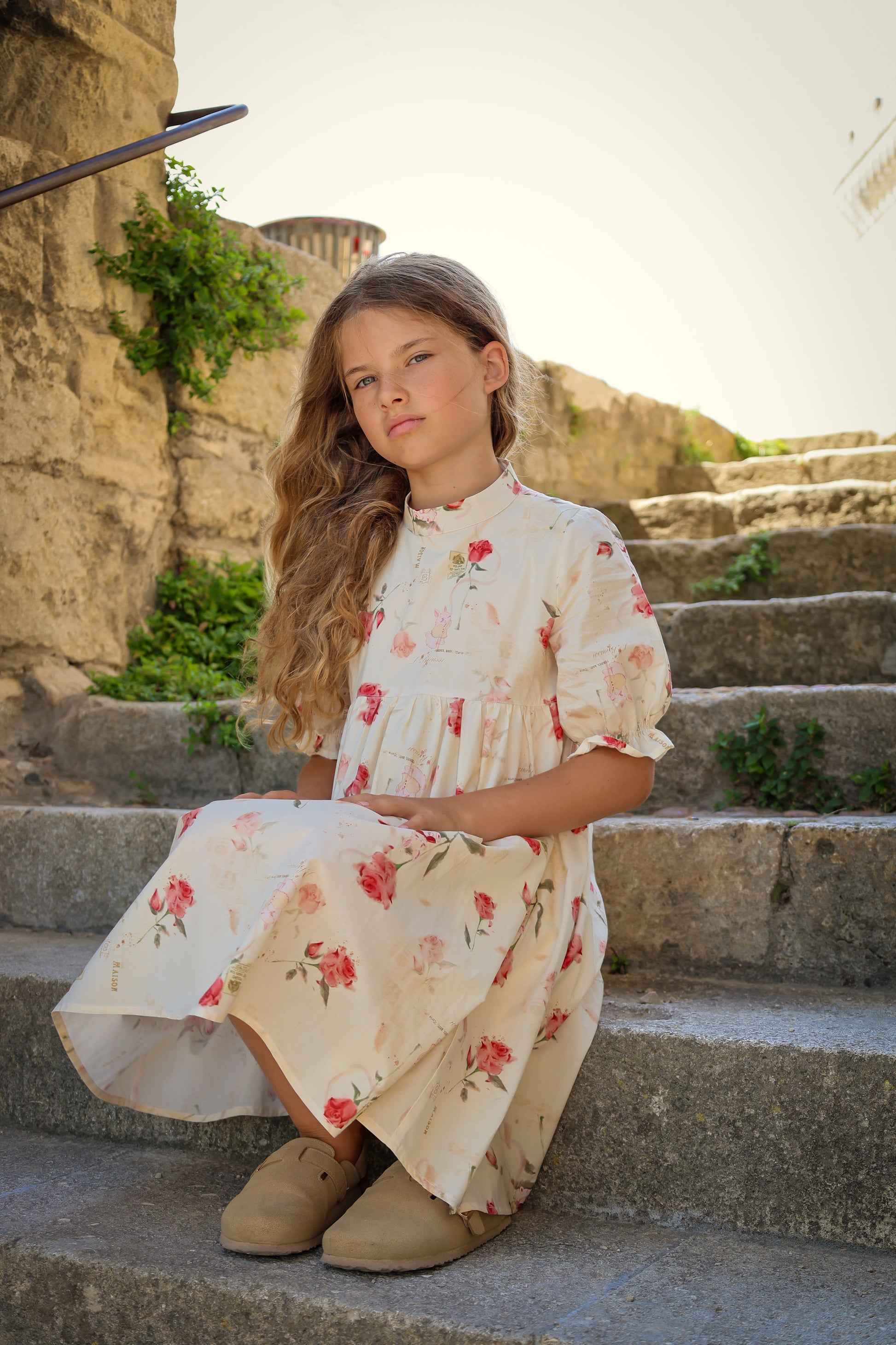 Young girl in a floral dress sitting on stone steps with a castle in the background