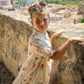 Young girl in a floral dress standing on a stone wall with a cityscape in the background
