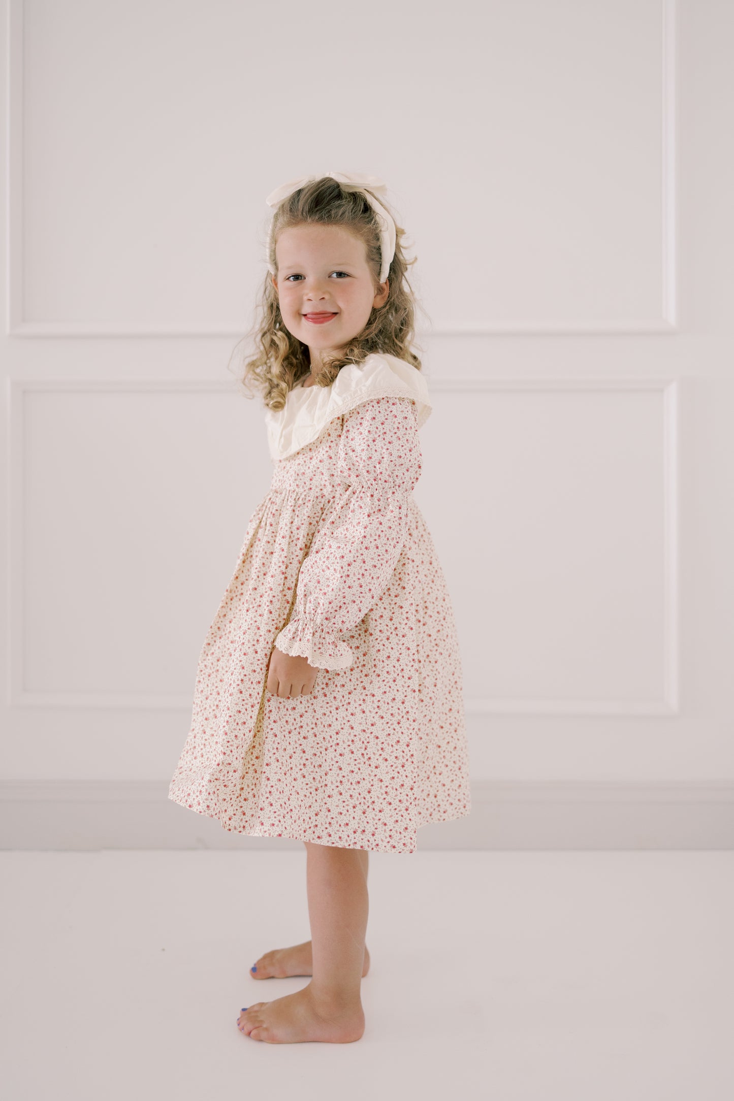 Young girl wearing a floral dress with a white headband against a light background