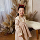 Young girl in a floral dress standing in front of decorative pampas grass and white curtains.