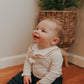 A baby wearing a white sailor-style collar bib with a knotted tie, sitting on the floor.