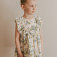 A young girl wearing a sleeveless, floral-print cotton dress with ruffled details.