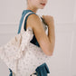 Young girl wearing a blue dress with a white floral backpack against a plain background